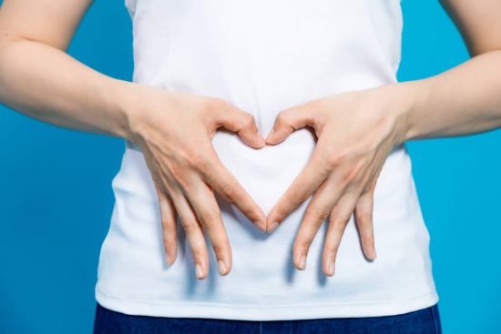Mujer tomándose su estómago y haciendo el gesto de un corazón con sus manos