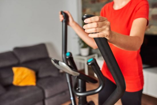 Mujer con elíptica en casa,, de fondo el sofá. Cardio en casa