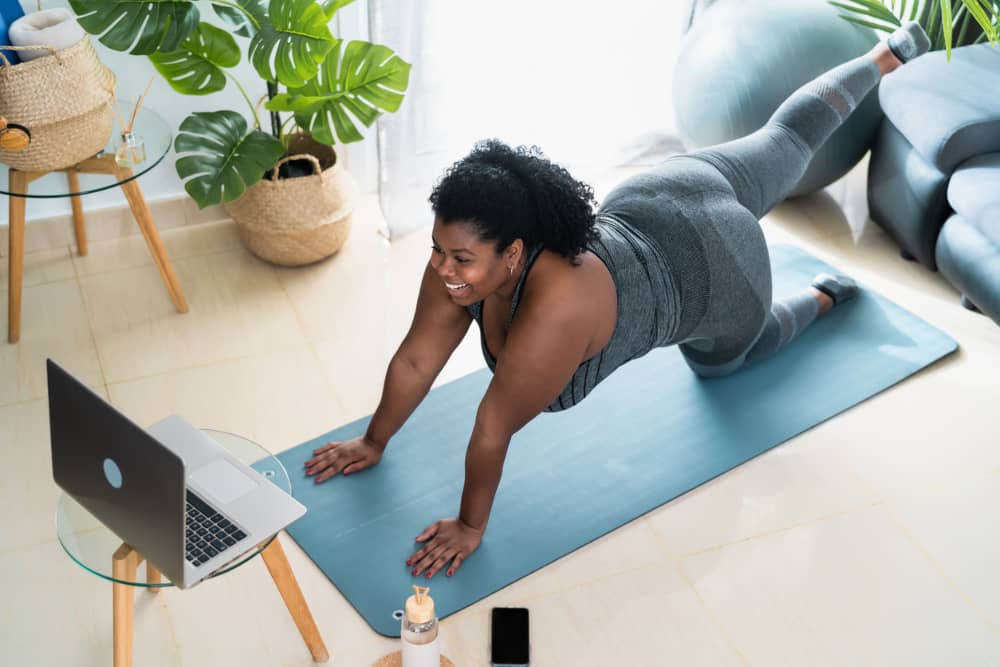 Mujer feliz realiza entrenamiento online frente a una laptop. 