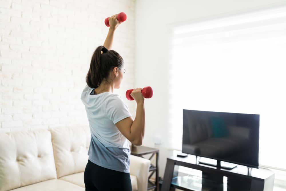 Mujer entrena ejercicios de hombros en casa con mancuernas